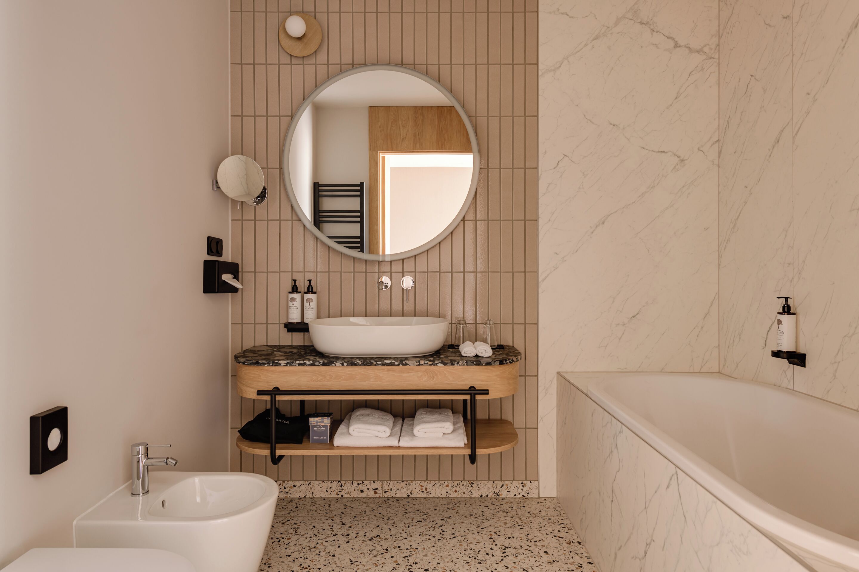 Une salle de bain moderne avec une baignoire sur pied, un lavabo sur pied, un miroir rond et un porte-serviettes.