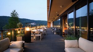 A balcony with outdoor seating, large windows, and a view of a forested area. - BELMONTE Hotel Krynica-Zdrój (Krynica-Zdroj)