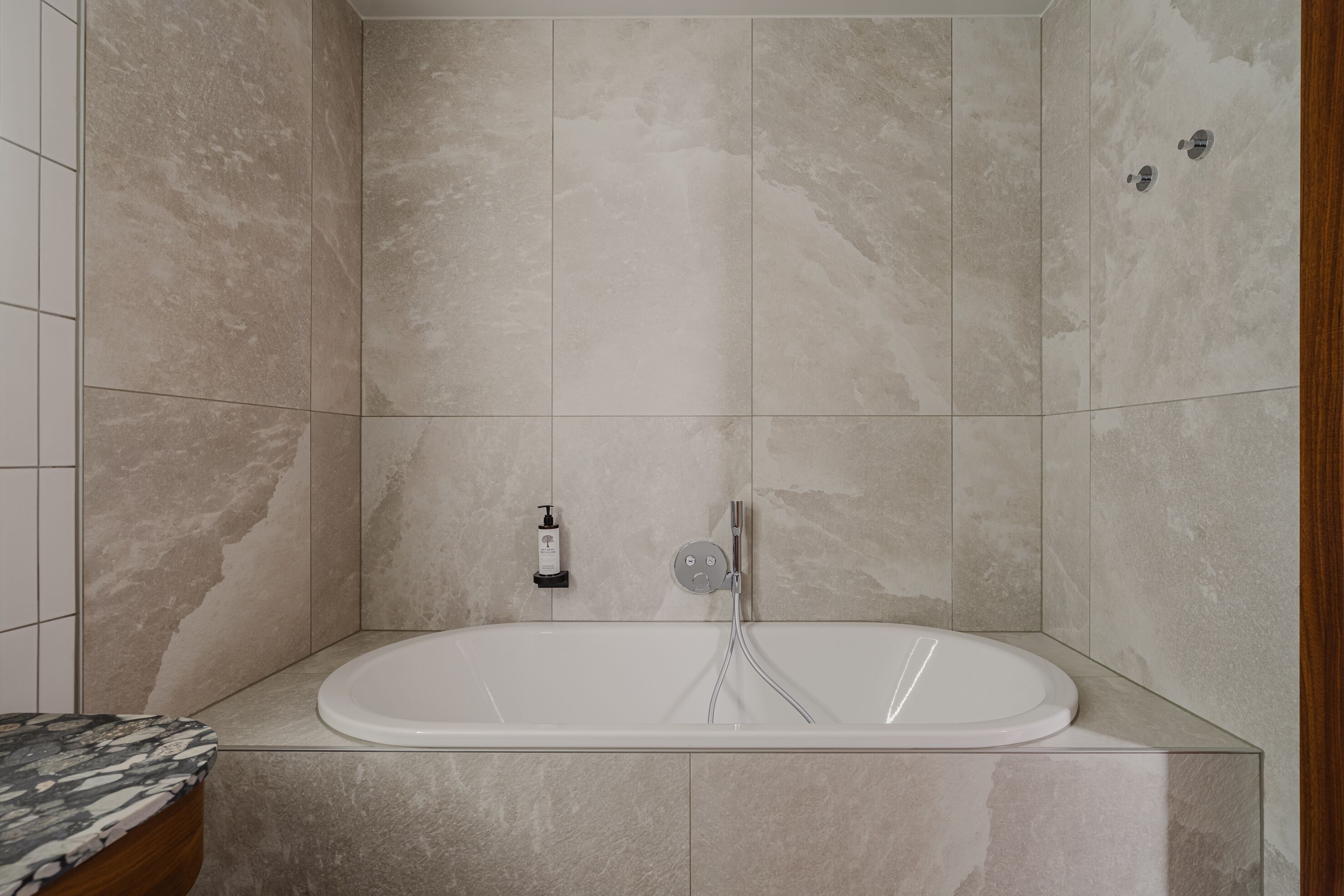 Un baño moderno con una bañera independiente, encimera de mármol y dispensador de jabón en la pared.