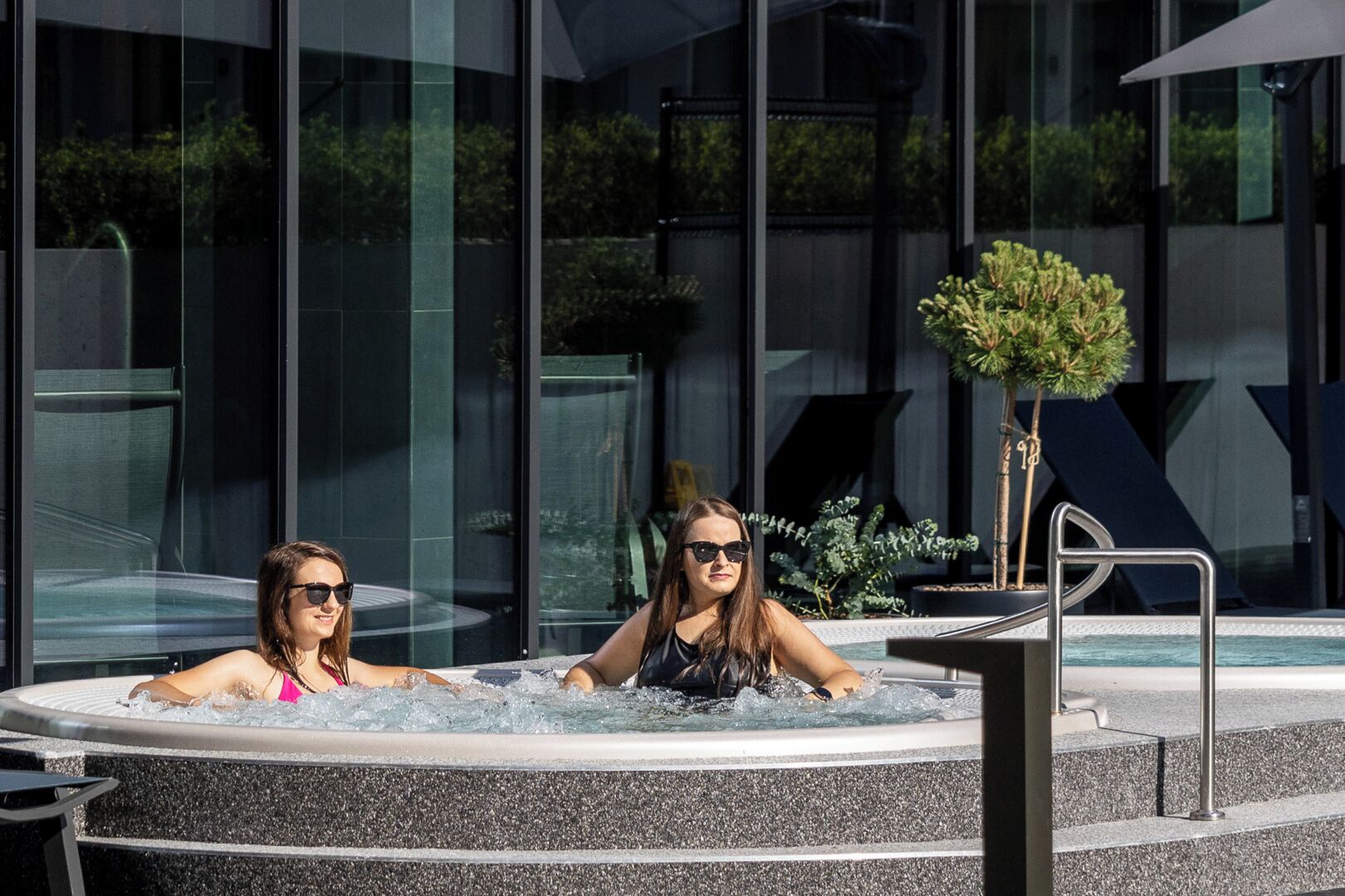 Two people in a hot tub with a modern building in the background.