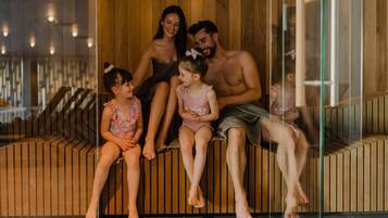A family of four seated on a wooden bench in a modern, well-lit indoor space with a wooden wall and glass partition.