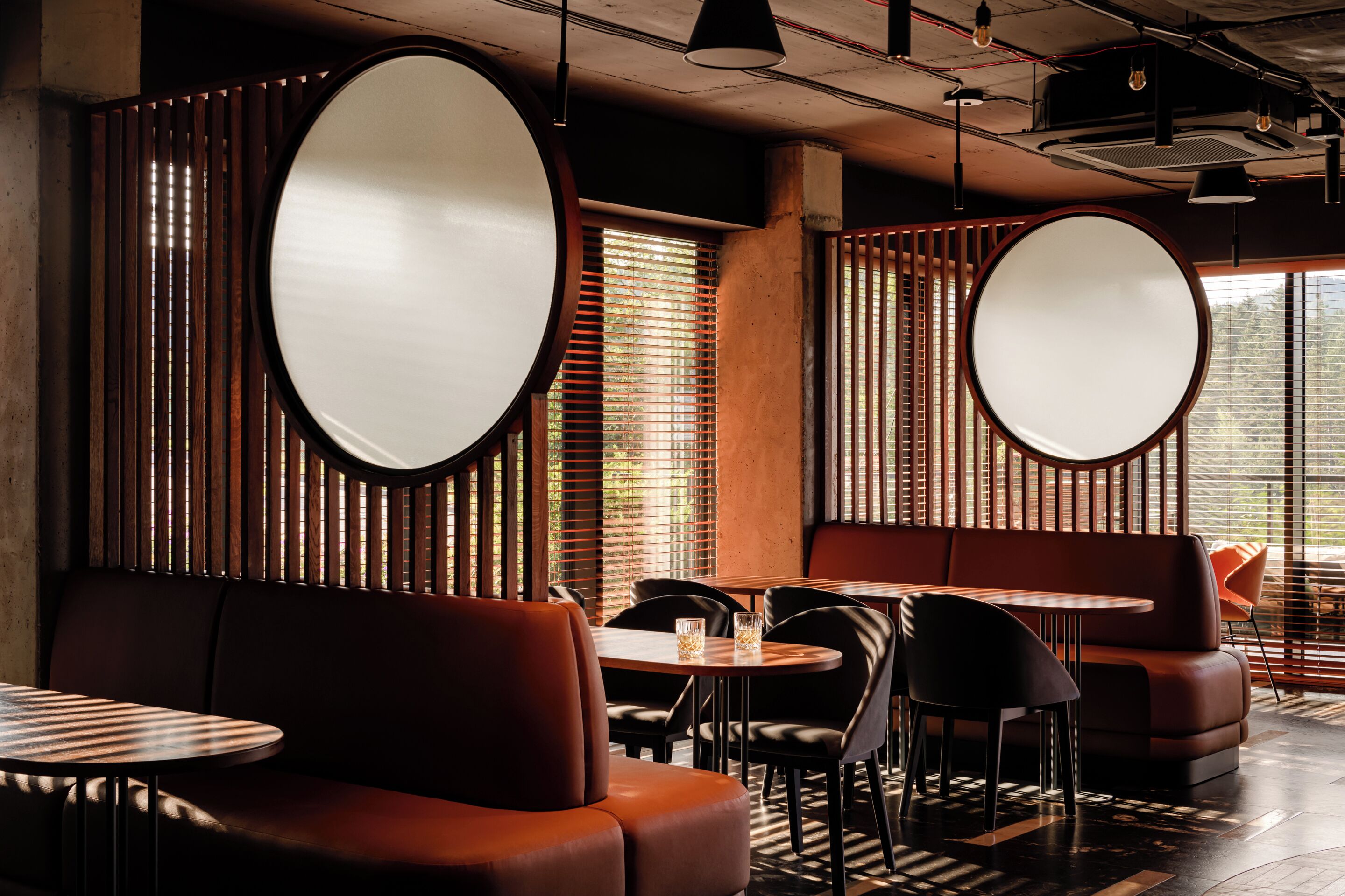 Un interior de restaurante con mesas redondas, cabinas y un diseño moderno.