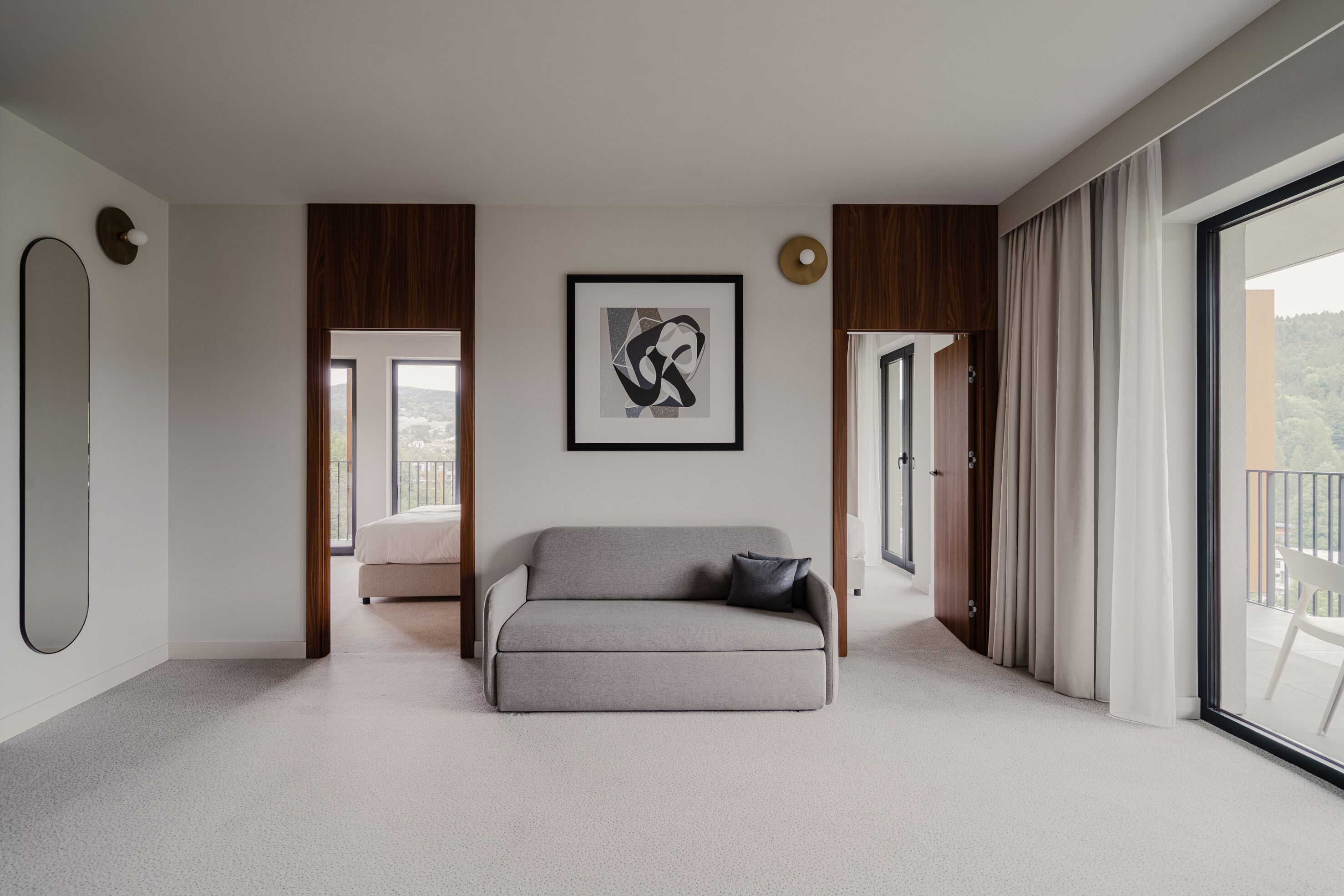 A modern living room with a grey sofa, a framed abstract artwork, and a large window with curtains.