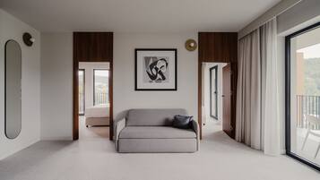 A modern living room with a grey sofa, a framed abstract artwork, and a large window with curtains.