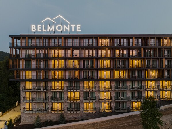 Un hotel de varios pisos con un llamativo letrero 'BELMONTE', que cuenta con balcones con mobiliario exterior y fachada de piedra.