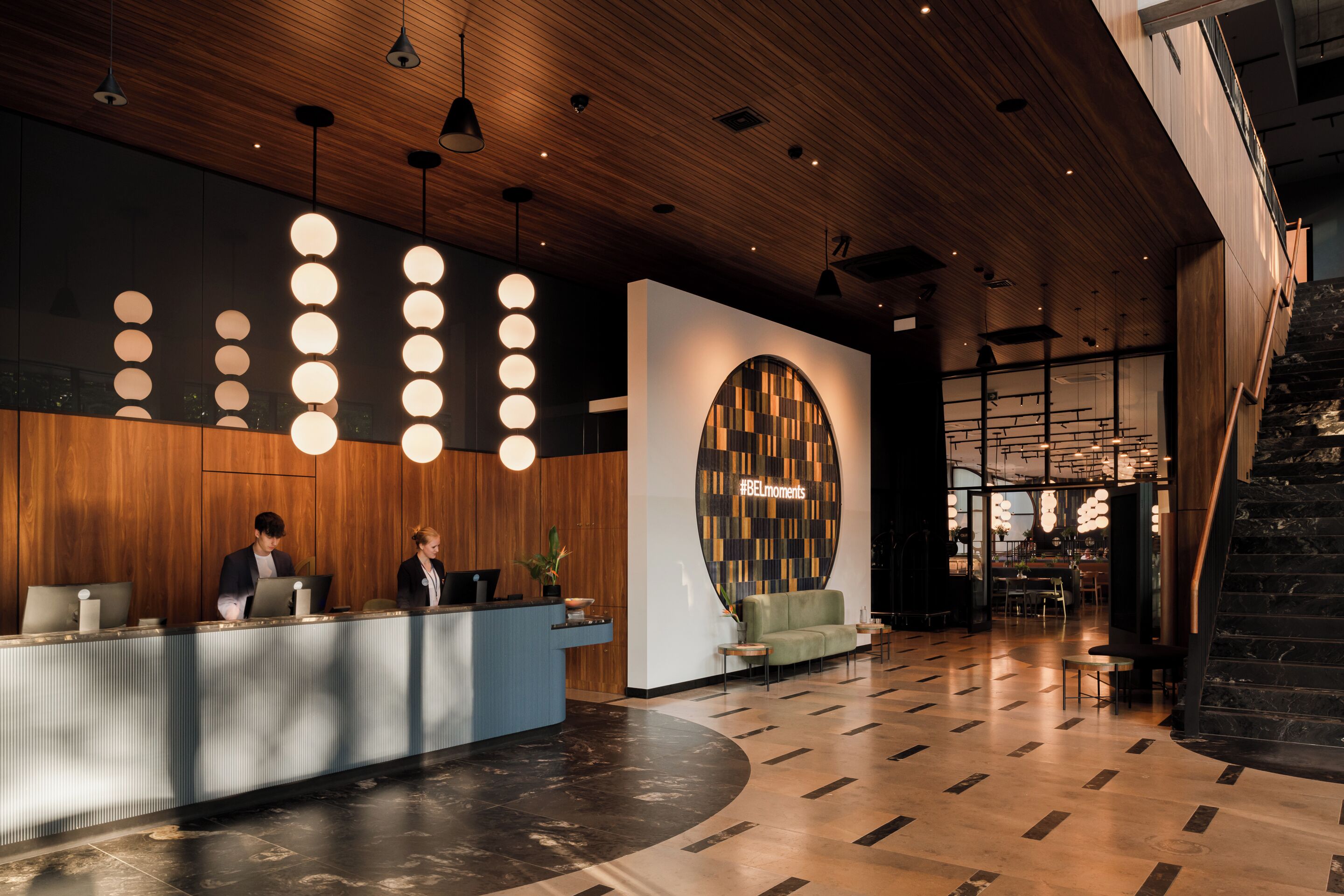 A modern reception area with a wooden reception desk, a large circular wall design, and a staircase leading to upper floors.