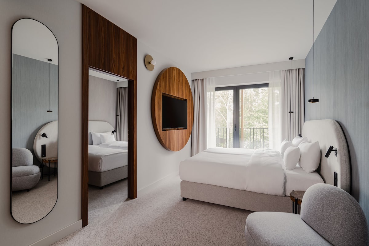Une chambre d’hôtel moderne avec un grand lit, un téléviseur fixé au mur et un grand miroir.