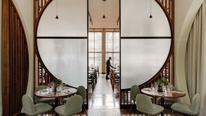 A restaurant with round tables, chairs, and a person walking in the background. - BELMONTE Hotel Krynica-Zdrój (Krynica-Zdroj)