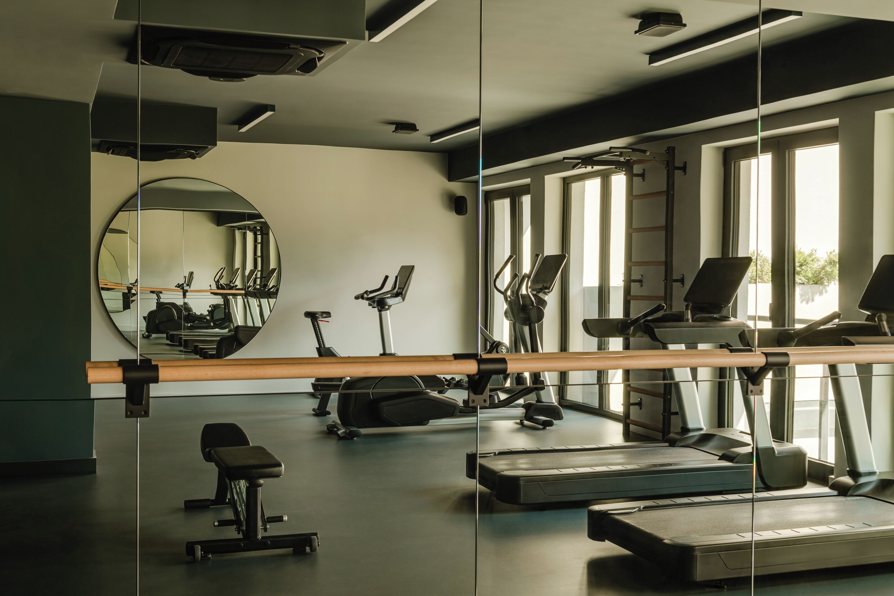A gym with exercise equipment, a large mirror, and windows.