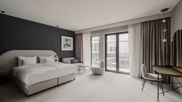 Quarto de hotel moderno com uma cama grande, um sofá, uma escrivaninha e uma cadeira. Há uma janela ampla com cortinas e vista para o exterior.