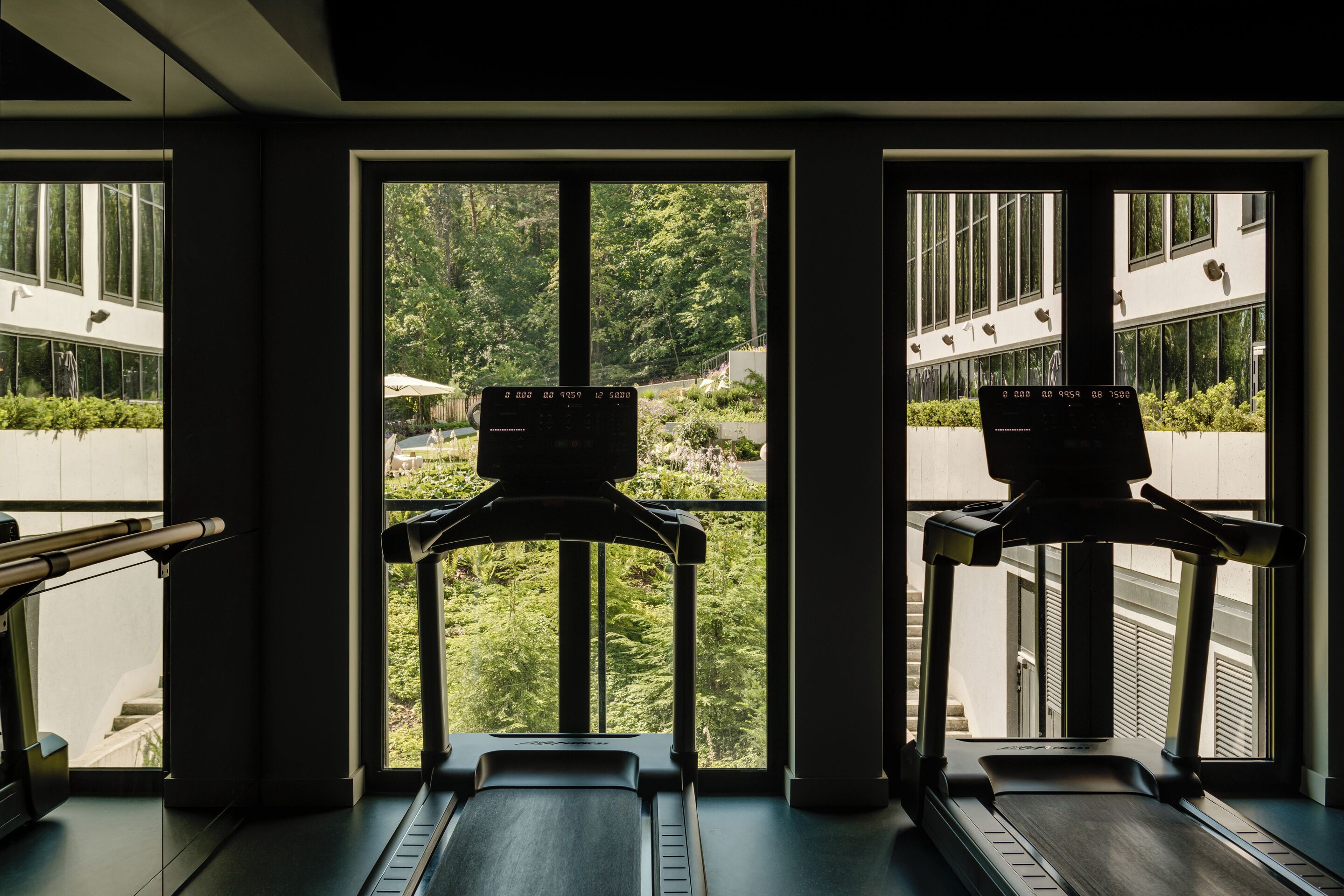 Un gimnasio con cintas de correr y vistas a un edificio y áreas verdes al exterior.