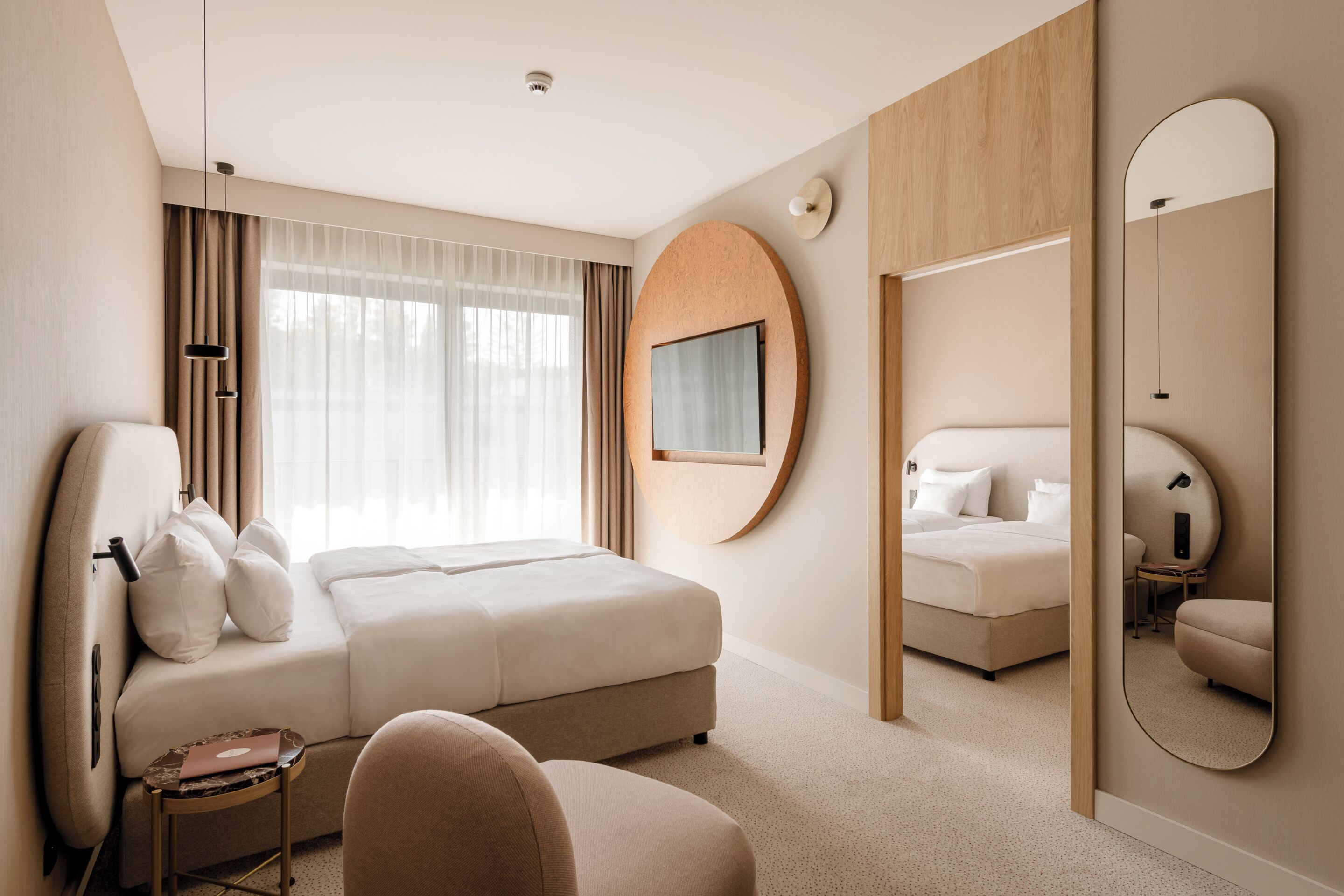 A modern hotel room with a large bed, a sitting area, a small table, and a mirror.