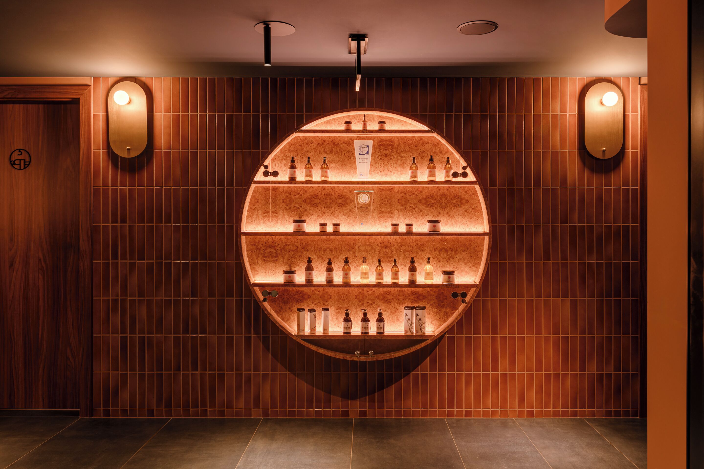 Un présentoir circulaire mural, composé de différentes bouteilles, probablement une sélection de boissons alcoolisées, dans une pièce aux murs lambrissés et dotée d’un éclairage encastré.