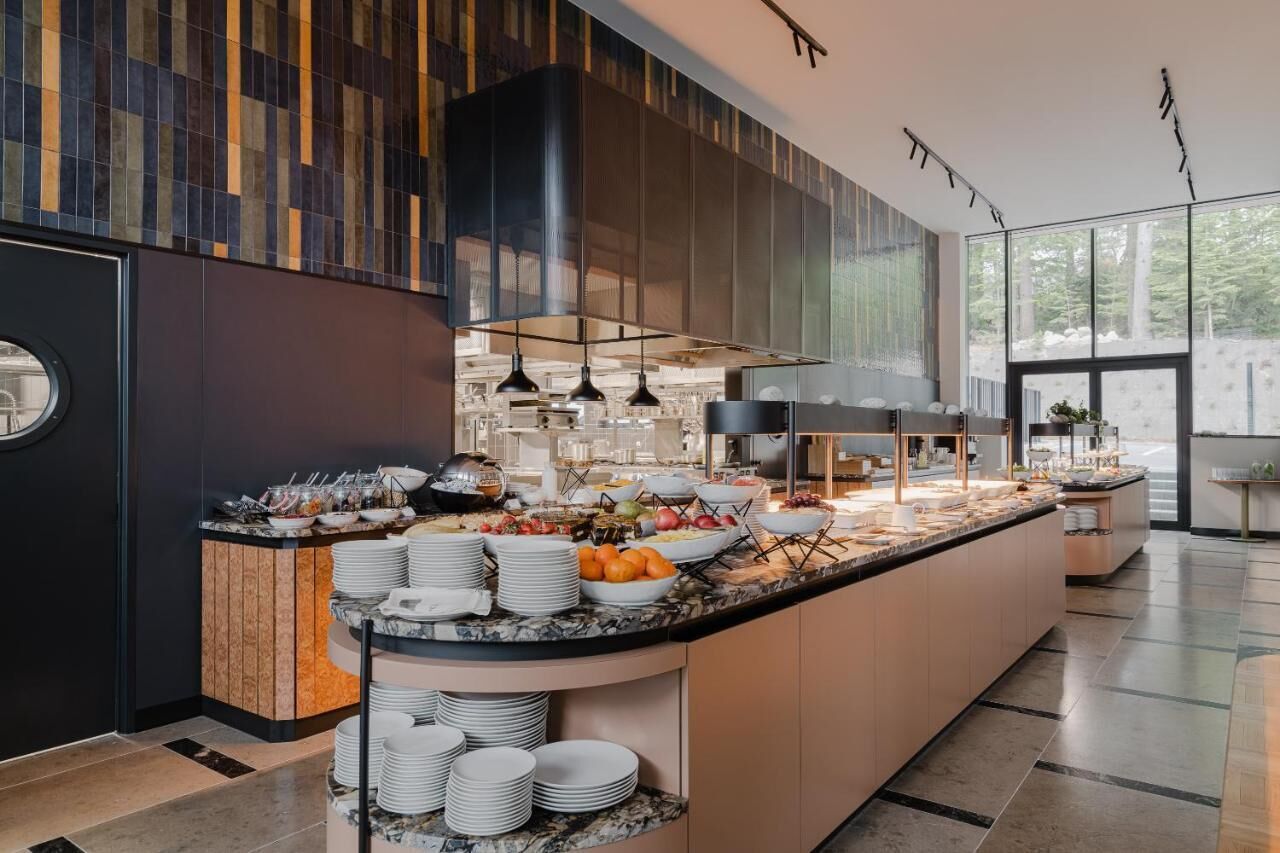 A modern kitchen with a marble countertop, a buffet setup, and a large window providing a view of the outdoors.