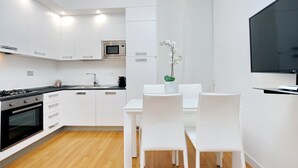 A modern kitchen with white cabinetry, a built-in microwave, a gas stove, and a dining area with white chairs and a table. - DEZA cozy place Piazza del Popolo 2 (Roma)