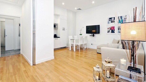 A modern living room with a wooden floor, white furniture, a flat-screen TV, and a dining area with a white table and chairs. - DEZA cozy place Piazza del Popolo 2 (Roma)