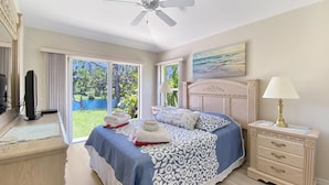 Quarto de hotel com cama, escrivaninha, luminária, ventilador de teto e vista para o exterior.