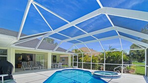 Piscina exterior coberta com hidromassagem, rodeada por um terraço com cadeiras e mesa.
