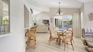 Ampla sala de estar com mesa de jantar cercada por cadeiras de vime, um sofá e um ventilador de teto.