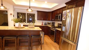 A modern kitchen with wooden cabinets, a stainless steel refrigerator, a built-in oven, and a large island with bar stools. - Remodeled one story pool home, hiking trails, lake, beach & more.. (Agoura Hills)