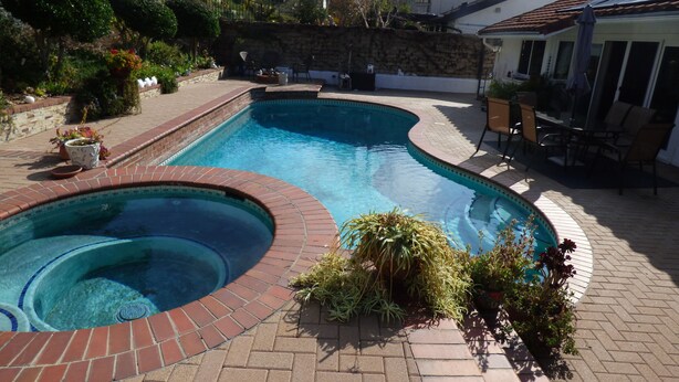 A swimming pool with a brick edge, surrounded by a patio with potted plants and outdoor furniture. - Remodeled one story pool home, hiking trails, lake, beach & more.. (Agoura Hills)