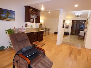A living room with a brown leather chair, wooden flooring, a kitchen area with a wine rack, and a dining area with a table and chairs. - Remodeled one story pool home, hiking trails, lake, beach & more.. (Agoura Hills)