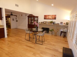 A spacious living area with a wooden floor, a dining table with chairs, a fireplace, and a wall with framed pictures.