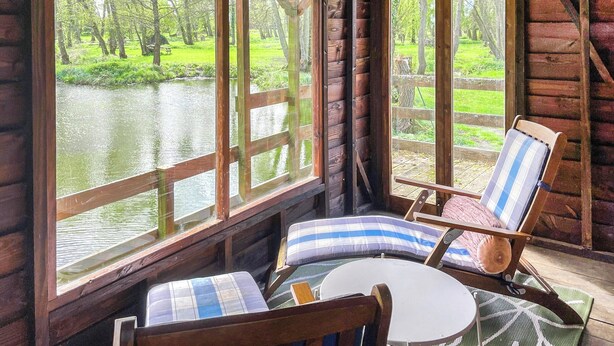 A cabin with large windows overlooking a river, wooden furniture, and a rustic interior. - 3 bedroom accommodation in North Walsham (North Walsham)