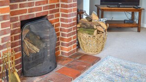 A fireplace with a fire screen, a wicker basket with firewood, a television on a stand, and a patterned rug on the floor. - 3 bedroom accommodation in North Walsham (North Walsham)