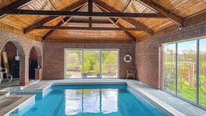 An indoor swimming pool with a wooden ceiling and brick walls, large sliding glass doors leading to a garden. - 3 bedroom accommodation in North Walsham (North Walsham)