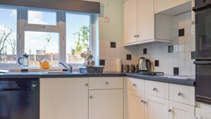 A modern kitchen with white cabinetry, a black dishwasher, and a window providing a view of the outdoors. - 3 bedroom accommodation in North Walsham (North Walsham)