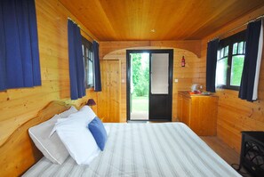 Een houten kamer met een bed, een klein keukentje en een deur naar buiten.