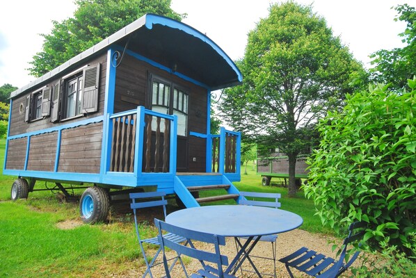 Een houten huis met een blauwe gevel, een veranda en een tafel met stoelen ervoor.
