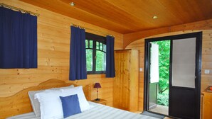 A wooden cabin bedroom with a bed, curtains, a nightstand, and a door leading to a balcony.