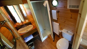 A wooden cabin bathroom with a shower, toilet, sink, and a mirror.