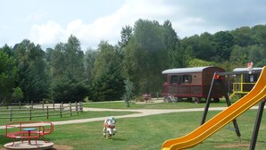 A playground with a yellow slide, a merry-go-round, and a small train-themed playhouse.