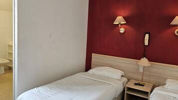 Ein Hotelzimmer mit zwei Einzelbetten, einem Holz-Kopfteil, einer roten Akzentwand und zwei Wandleuchten.