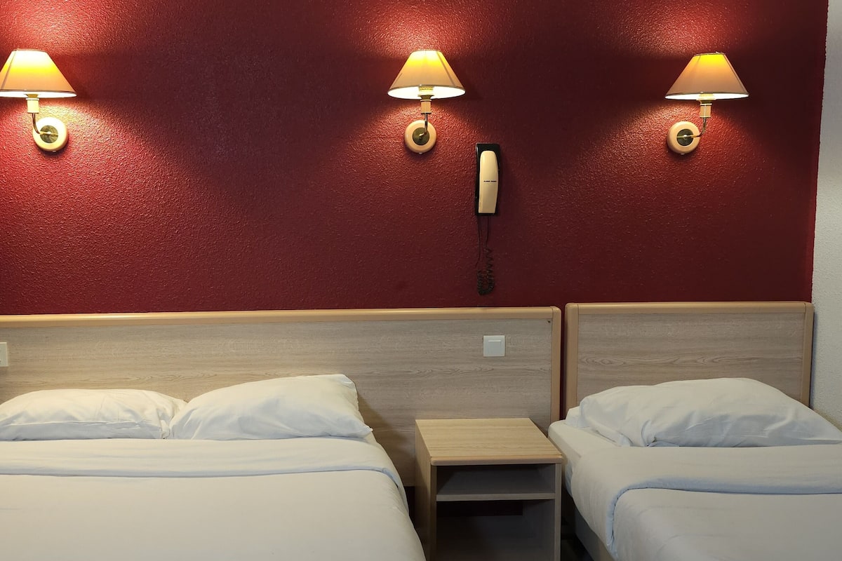 Ett hotellrum med två sängar, en sänggavel i trä och tre vägglampor.