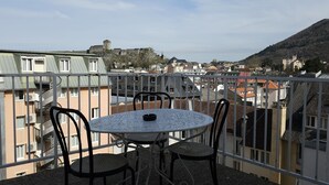 A balcony with a round table and chairs, overlooking a cityscape with buildings and a hill. - Hotel CORONA Lourdes (Lourdes)