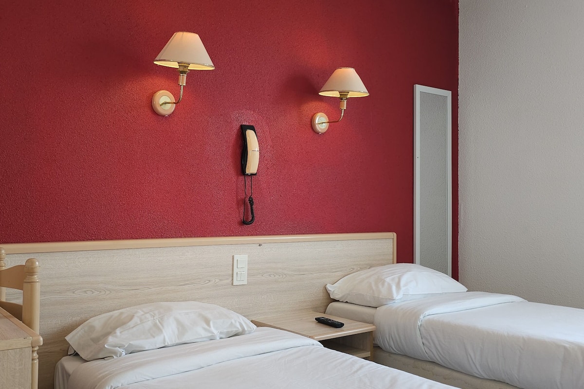Ett hotellrum med två sängar, en sänggavel i trä, ett skrivbord med en lampa och två väggmonterade lampor.