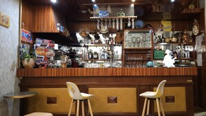 A bar area with wooden decor, shelves of bottles, and two stools. - Hotel CORONA Lourdes (Lourdes)