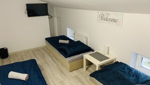 A room with two beds, a small table, a radiator, a TV, and a 'Welcome' sign. - charming Cataleya hostel in a quiet and beautiful neighborhood (Lublin)