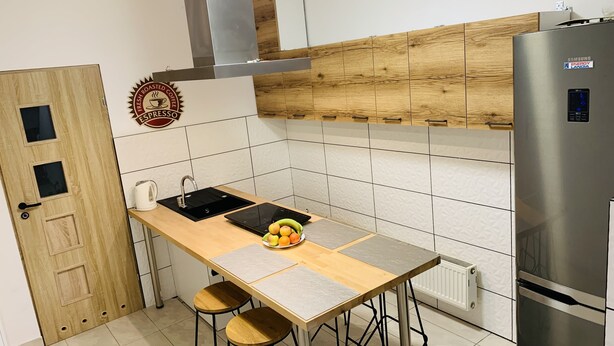 A modern kitchen with a wooden door, a stainless steel refrigerator, a kettle, and a fruit bowl on the counter. - charming Cataleya hostel in a quiet and beautiful neighborhood (Lublin)
