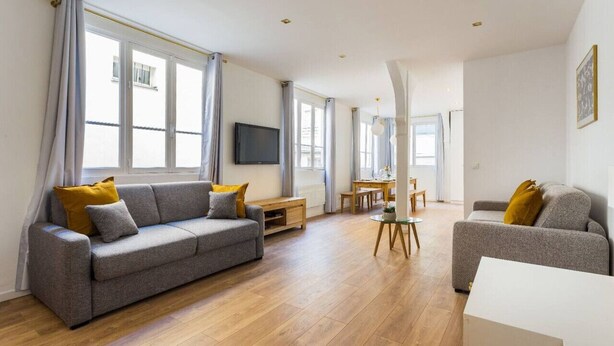 A modern living room with a grey sofa, a coffee table, and a dining area with a table and chairs. - Appartement8P/Full Equipped/Bonnenouvelle/Bourse (Paris)