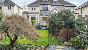 A residential property with a well-maintained garden, a patio with outdoor furniture, and a large house with multiple windows and a chimney. - 3 bedroom accommodation in Keswick (Keswick)