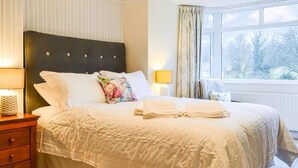 A neatly made bed with a floral pillow, a bedside lamp, and a view of a snowy landscape through a window. - 3 bedroom accommodation in Keswick (Keswick)