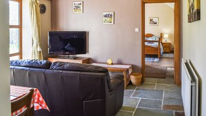 Een gezellige woonkamer met een grote flatscreen televisie, een bank en een eettafel met geruit tafelkleed.