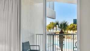 A balcony with a glass door, a pool, and palm trees in the background.