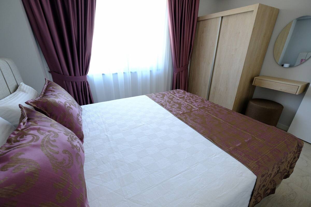 Una habitación de hotel con cama, armario, espejo y ventana con cortinas.