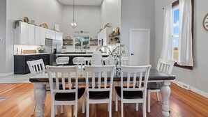Una cocina moderna con armarios blancos, una isla central y un comedor con sillas blancas y una mesa oscura.